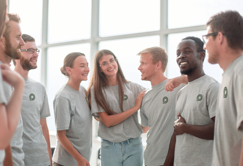 Einige Teamkolleg*innen stehen lächelnd beisammen und tragen alle das gleiche graue Shirt mit Firmenlogo